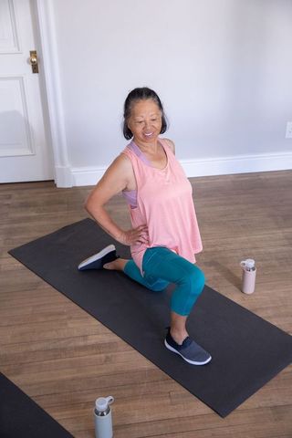Senior asian woman stretching in deep lunge on mat in bright home studio for fitness