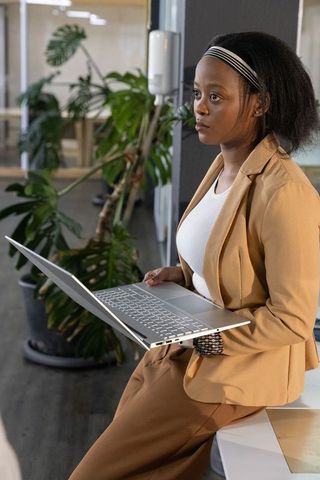 African american businesswoman holding laptop in modern coworking office with greenery