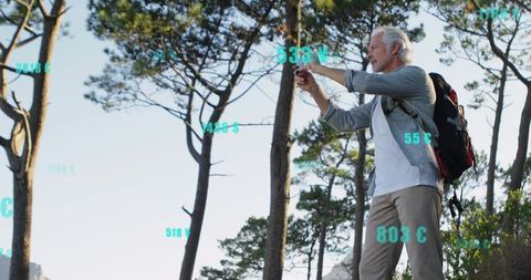 Senior hiker capturing trail with smartphone and teal data overlays on hillside