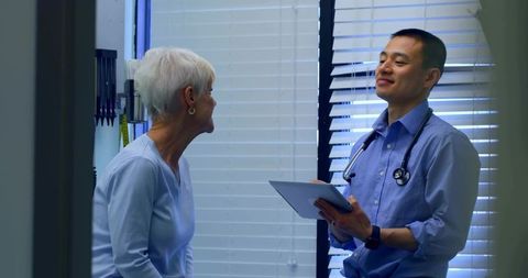 Primary care physician consulting senior woman using tablet and stethoscope in clinic