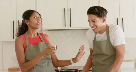 African American couple cooking together in bright modern kitchen laughing and measuring