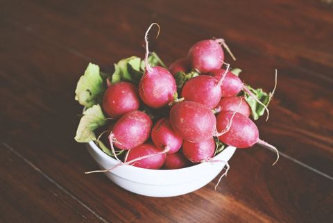 Fresh red radishes in white bowl on rustic wood table organic produce still life