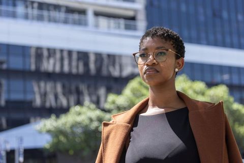 Confident professional woman standing in urban plaza wearing brown coat and eyeglasses