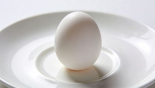 Minimalist white egg standing on glossy porcelain plate with soft reflection