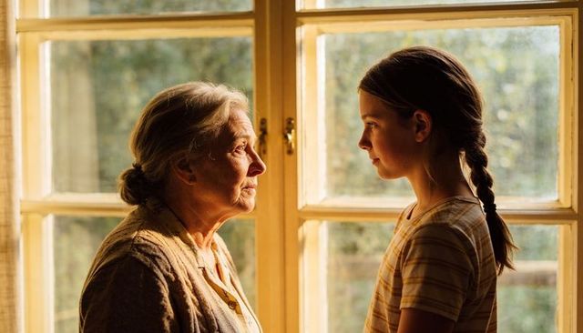 Grandmother and granddaughter sharing tender moment by window in warm golden light