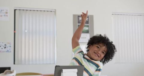 Excited student raising hand in classroom with tablet stand smiling and engaging in learning