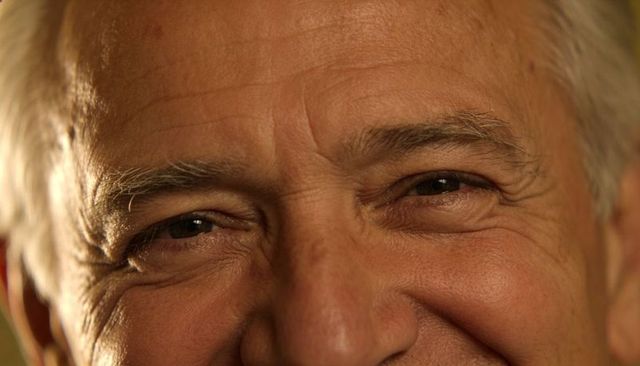 Smiling senior man closeup featuring deep forehead lines, crow's feet and warm studio highlights