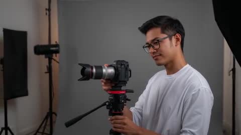 Asian photographer adjusting DSLR on tripod in studio preparing portrait shoot
