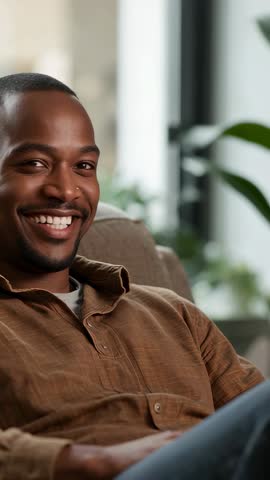Man Lifting Chin and Grinning on Couch in Casual Brown Shirt Vertical Lifestyle Video
