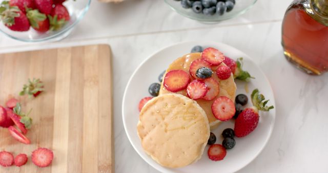 Fresh pancakes topped with strawberries and blueberries, drizzled with honey syrup. Ideal for use in food blogs, recipe books, breakfast and brunch menu designs, diet and nutrition presentations, or healthy eating campaigns.