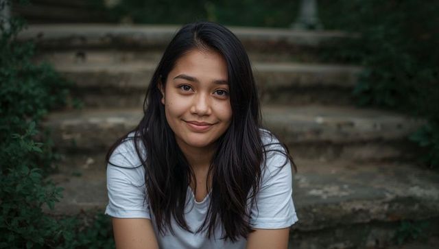 Smiling young woman sitting on worn stone steps in garden, natural outdoor portrait