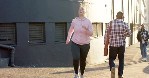 Woman Jogging Past Commuters on Sunlit Urban Street - Morning Running, Active Lifestyle