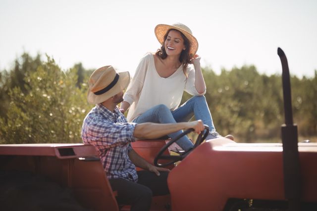 Happy young couple sitting together on tractor at olive farm