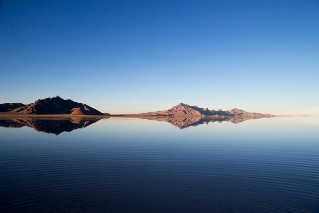 This image shows tranquil mountain reflections on a calm lake under a clear sky, perfect for decorating office spaces, nature magazines, travel brochures, and backgrounds for computer screens to evoke a sense of tranquility and natural beauty.
