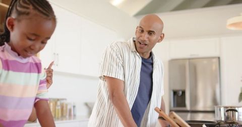 Indian father guiding african american child cooking together in bright modern kitchen