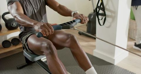 Pulling seated row machine in home gym with kettlebells, cable resistance, smartwatch