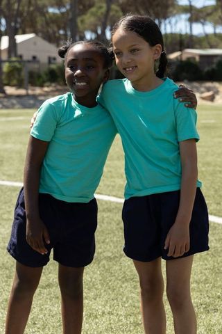 Diverse preteen girls embracing on sports field wearing teal tops and navy shorts