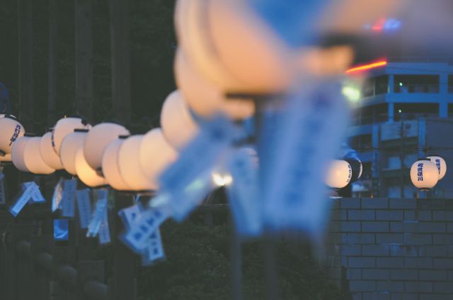 This image depicts glowing Japanese lanterns at night, creating a warm, soft light along a city street. The scene features a line of lanterns, which are out of focus, giving the photo a beautiful bokeh effect. Ideal for use in content related to Japanese festivals, night scenery, urban life, cultural events, or creating a serene and tranquil atmosphere in visual art or design projects.
