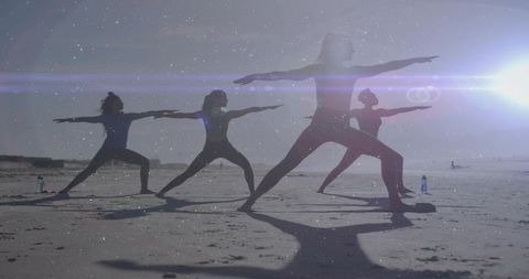 Practicing beach yoga at sunset with four women holding warrior poses backlit silhouettes