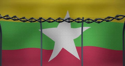 Myanmar flag behind razor wire and chain-link fence symbolizing border control restriction