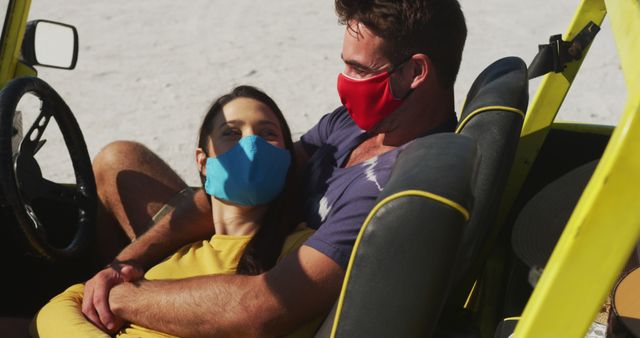 Happy caucasian couple wearing face masks sitting in beach buggy. beach stop off on summer holiday road trip during coronavirus covid 19 pandemic.