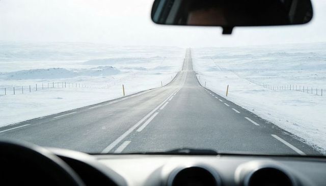 Driving toward distant horizon on snow-covered highway through remote winter plain