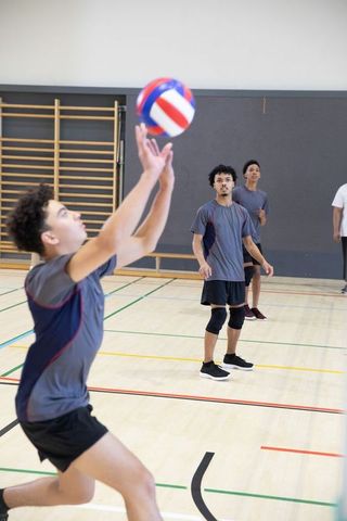Diverse teenage male volleyball team practicing placing and receiving ball on school gym court