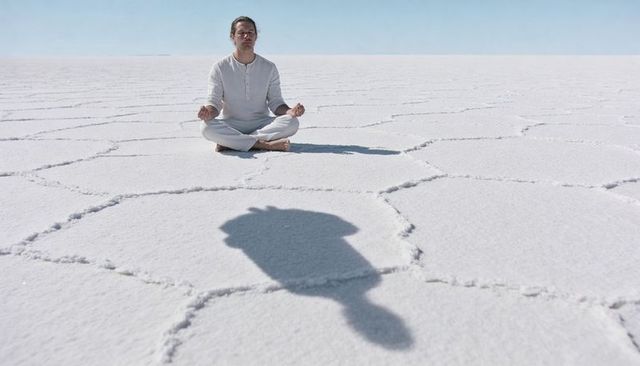 Meditating man on hexagonal salt flats in white robe barefoot embracing minimal calm