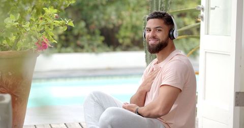 Relaxed Man with Headphones Seated by Poolside on a Wooden Deck