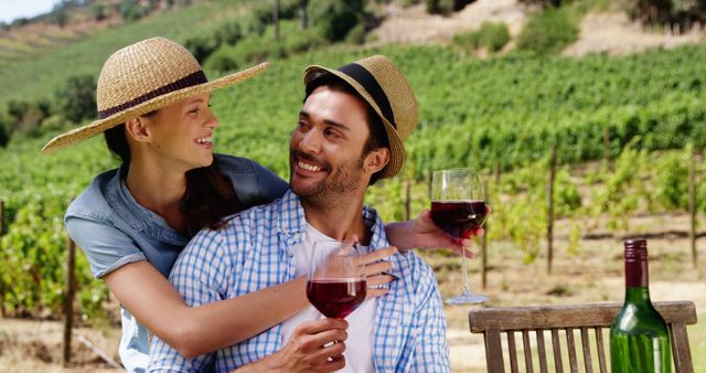 A young Caucasian couple enjoys a romantic moment with glasses of wine in a vineyard, with copy space. Their cheerful expressions and casual attire suggest a relaxed and intimate outing in a picturesque setting.