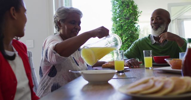 African american grandmother talking to her granddaughter while pouring juice in the glass. family, love and togetherness concept