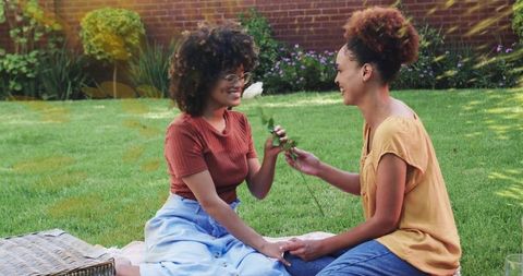 Smiling couple exchanging white rose during romantic backyard picnic, holding hands