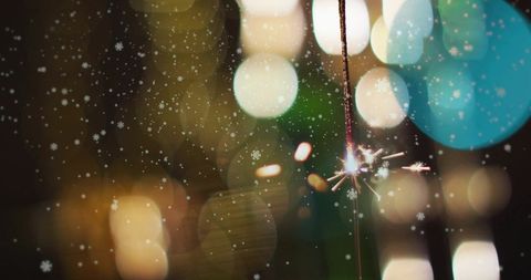 Festive sparkler with falling snowflakes and bokeh lights