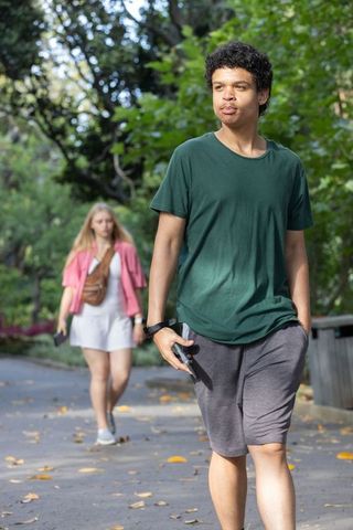 Young adults walking in leafy park holding smartphones enjoying sunny urban stroll