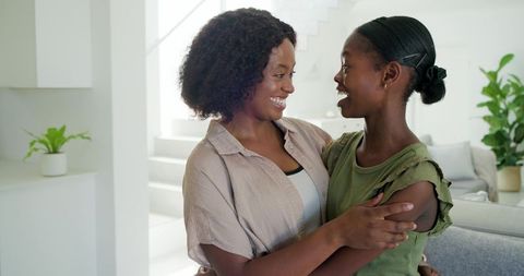 Joyful black mother embracing smiling daughter in bright modern living room with plants