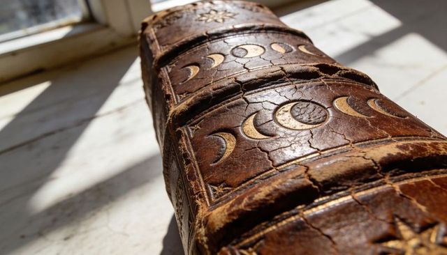 Antique leather book spine featuring embossed moon phases and star motifs in sunlight, worn patina