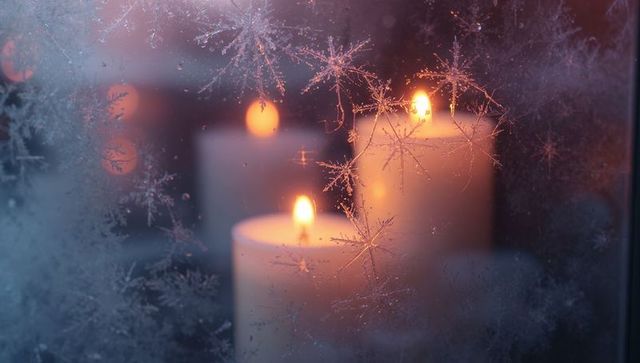 Glowing candles behind frost-covered window with snowflake crystals and warm bokeh