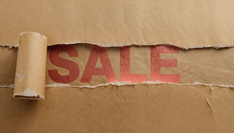 Kraft paper torn reveal showing bold red sale typography with rolled edge and texture