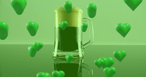 Floating green hearts surrounding clear glass mug of emerald beer with thick foam