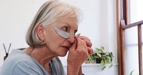 Senior woman peeling under-eye gel patch in relaxed home environment