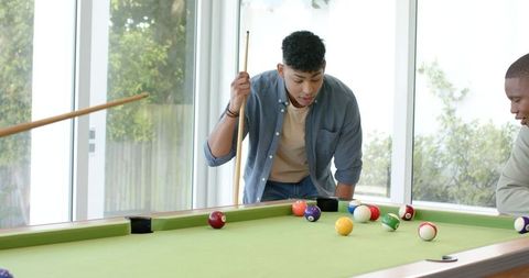 Diverse friends playing pool in bright home game room, casual leisure and social fun now