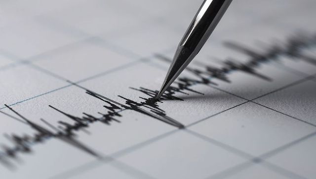 Seismograph stylus recording intense waveform on graph paper for data analysis