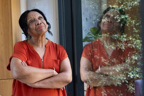 Contemplative senior african american woman looking out glass door with reflective garden mirroring