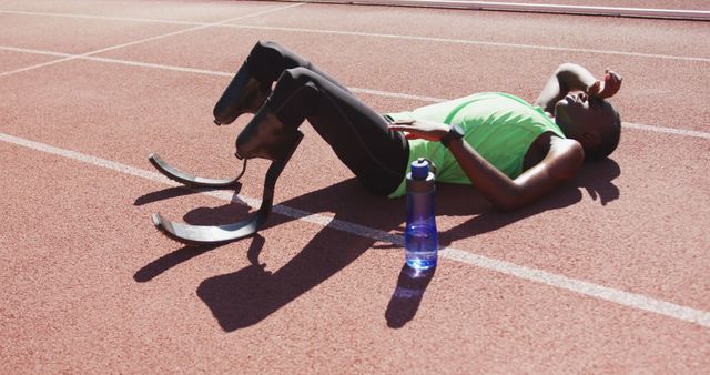 African american male athlete with prosthetic legs lying at empty stadium. Sport, disability, atletics and fitness, unaltered.