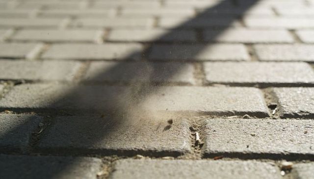 Sunlit concrete pavers with dust plume and diagonal shadow, closeup texture and pattern