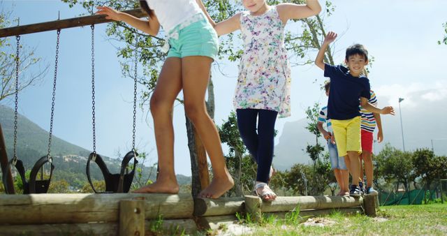 Children enjoying a sunny day on a playground, balancing on a wooden beam. This can be used for themes of outdoor activities, childhood fun, teamwork, diversity, and physical activity.
