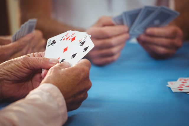 Senior citizens enjoying a card game at a retirement home, focusing on their hands holding cards. Ideal for use in articles or advertisements about senior living, retirement activities, community engagement, and leisure activities for the elderly.