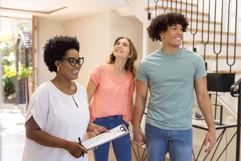 Couple touring modern home with african american realtor holding clipboard in bright foyer