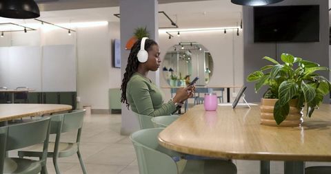 African american woman working remotely in coworking lounge with headphones and smartphone