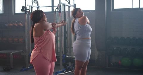 Diverse women stretching shoulders in gym warming up before workout, fitness partners